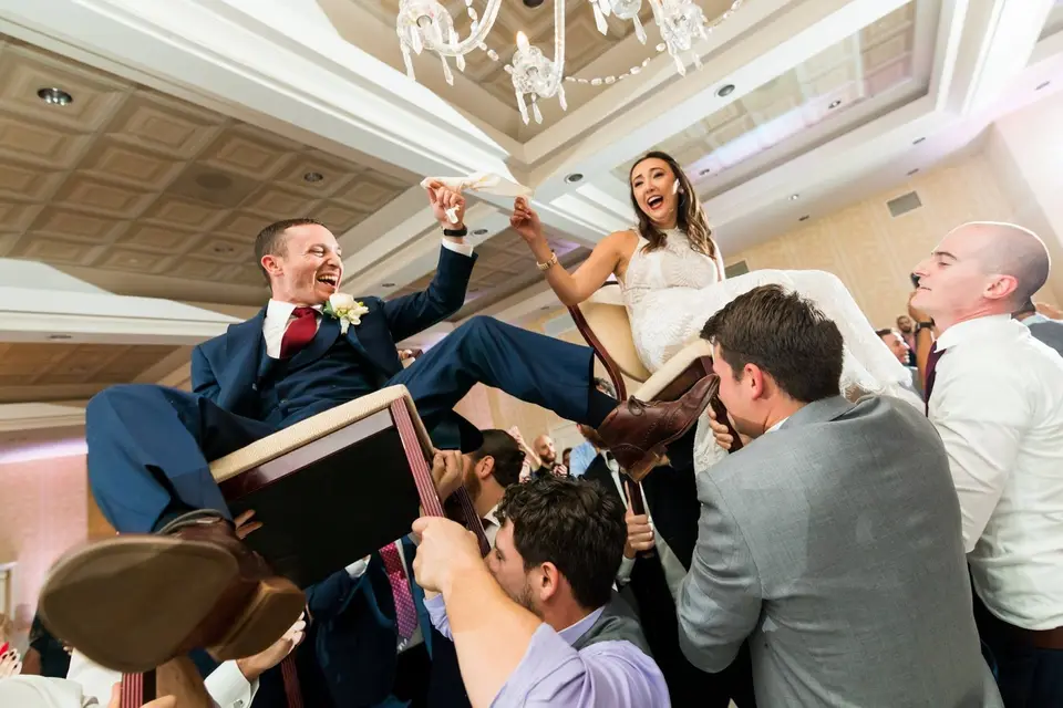 Groom and bride lifted on chairs by guests during a hora dance at a ballroom wedding reception