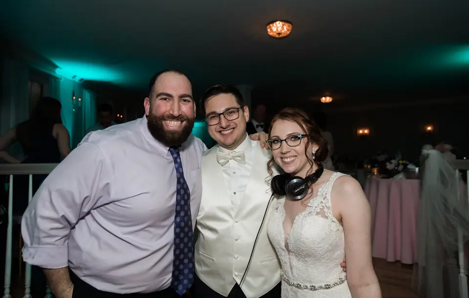 Two men and a bride wearing DJ headphones posing together at a reception