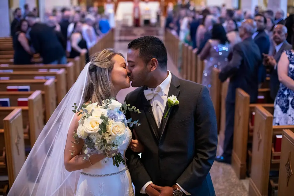 Bride and groom kissing in the church aisle as guests stand in the pews behind them