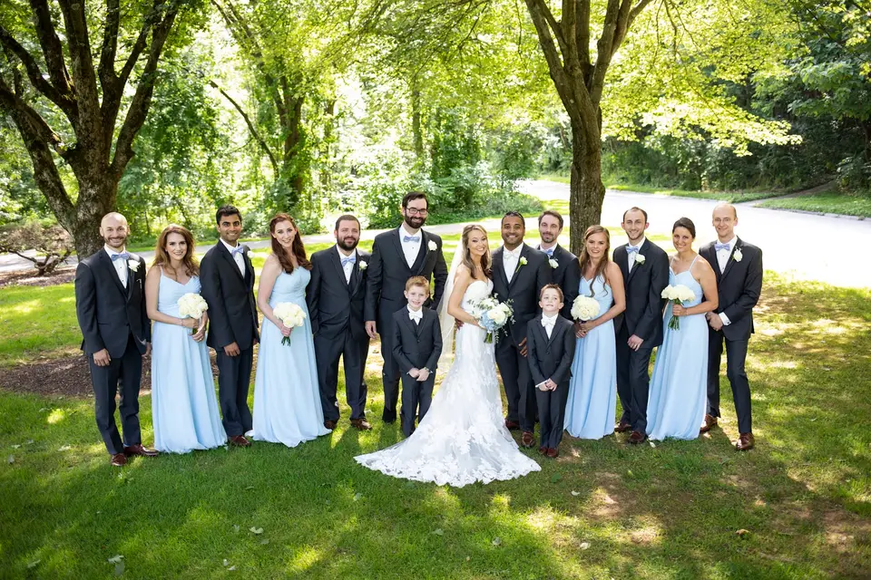 Atit and Maura with the wedding party, women in light blue dresses and men in gray suits, on a shaded lawn