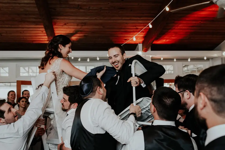 Groom and bride lifted on chairs during the hora, with guests in white shirts holding them up