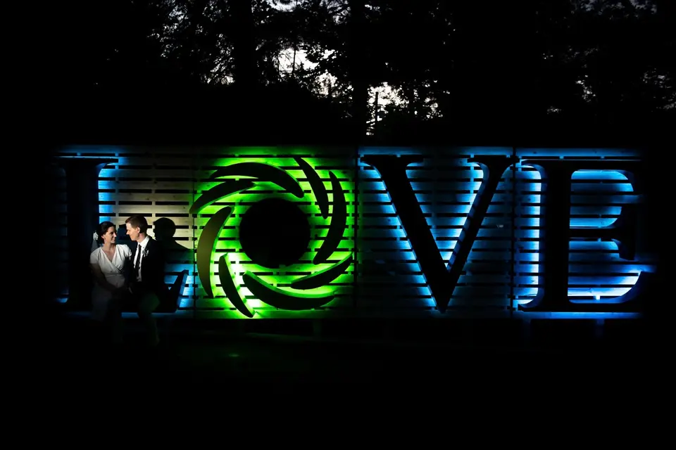 Bride and groom posing in front of lit-up LOVE letters at night