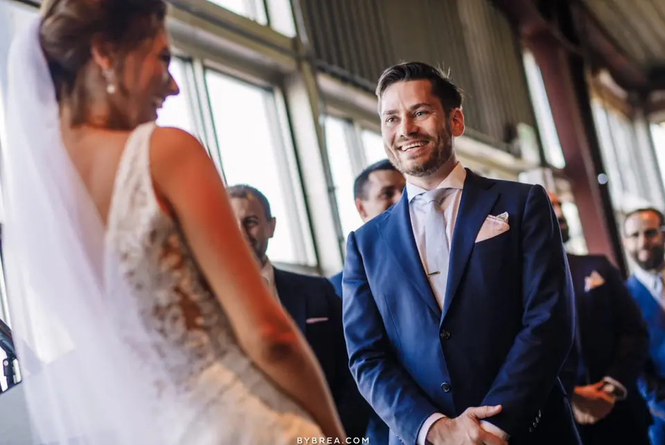 Smiling groom in a navy suit looking at the bride during the ceremony