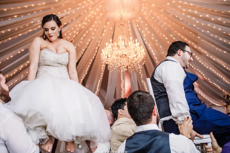 Bride and groom lifted on chairs by guests under a crystal chandelier at a Herrington on the Bay reception