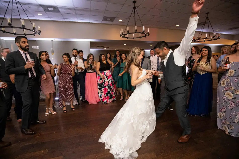 Bride and groom dancing as a crowd of guests in a banquet room cheer and watch
