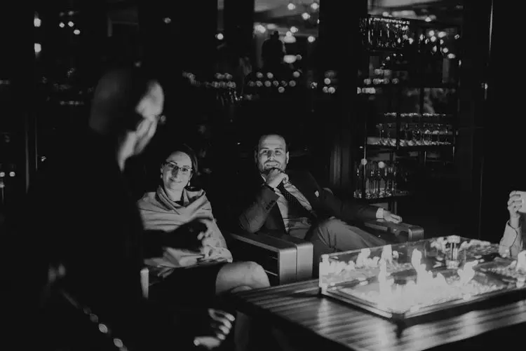 Black and white photo of guests relaxing around a fire table in a dimly lit lounge