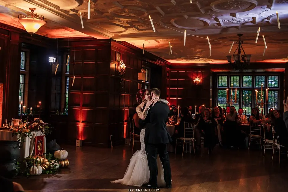 Bride and groom dancing in a wood-paneled mansion room with guests watching from tables