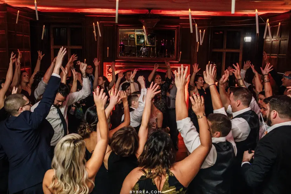 Wedding guests raising their hands and dancing in a crowded wood-paneled room