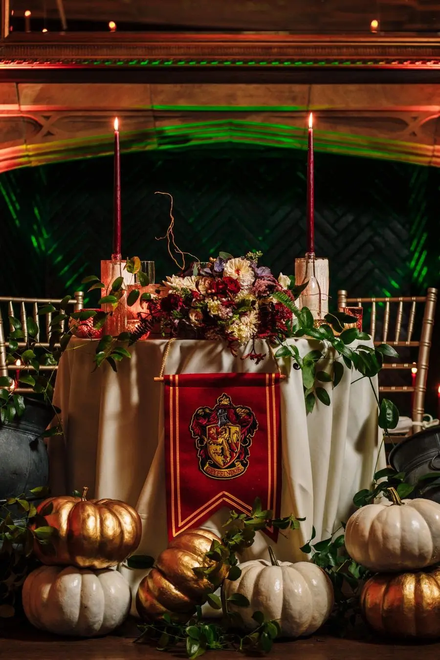 Sweetheart table with candles, flowers, a red house banner and gold and white pumpkins