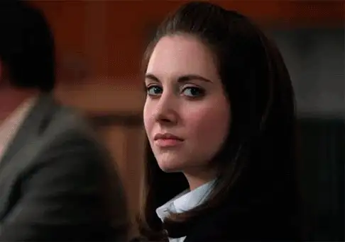Movie still of a woman with dark hair looking over her shoulder with a skeptical expression