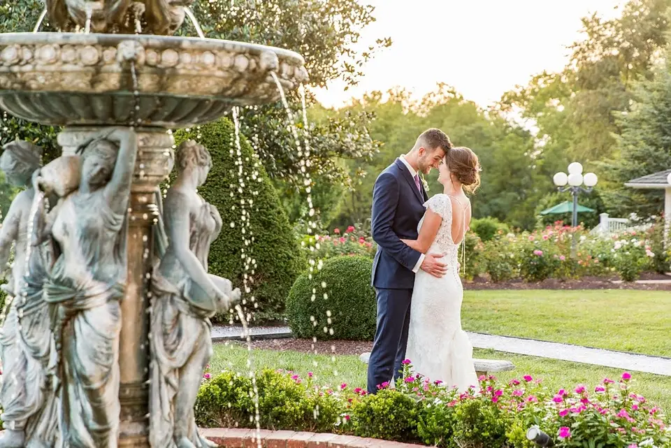 Couple embracing beside a stone fountain in a garden at sunset
