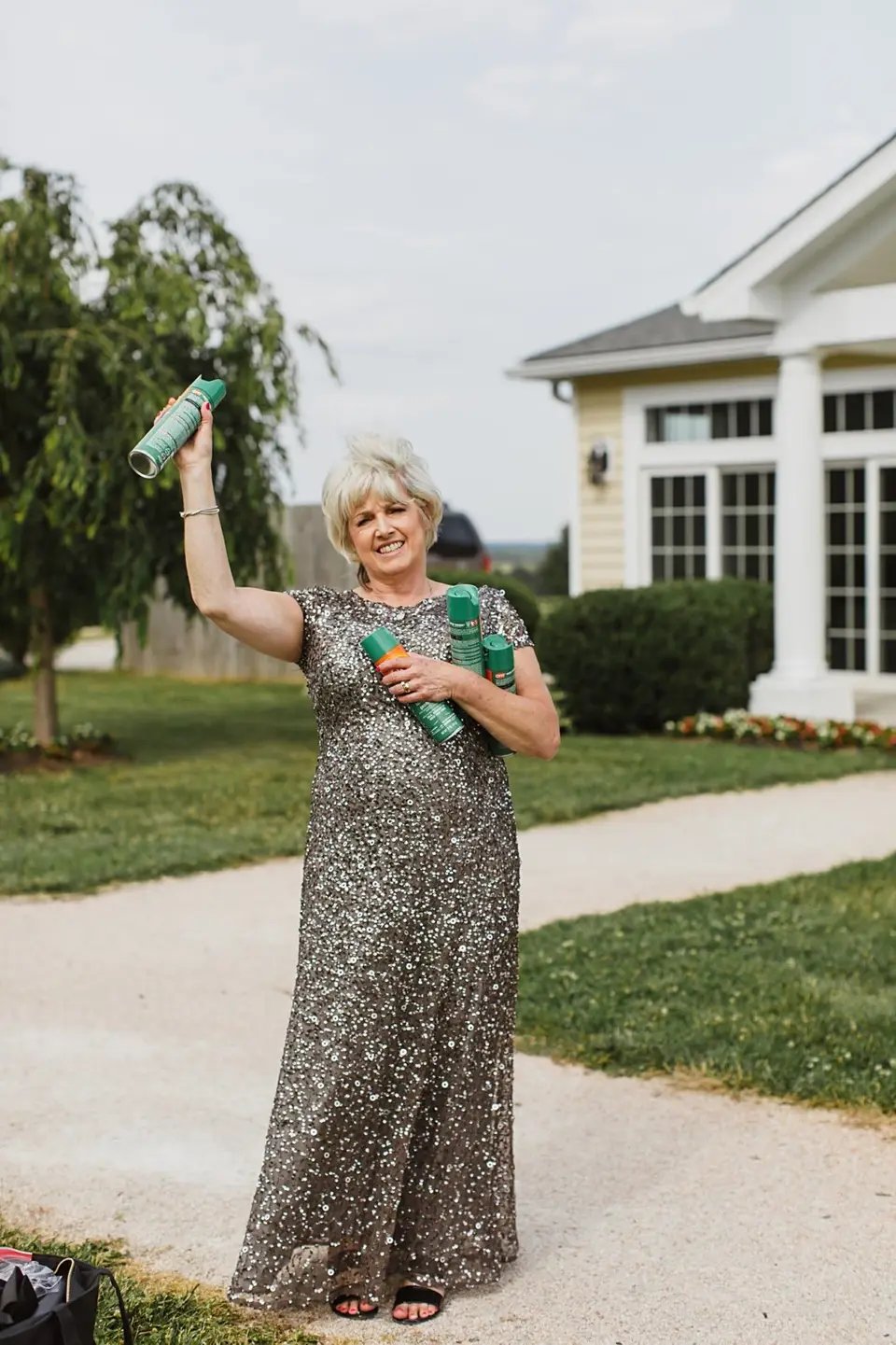 Woman in a sequined gown holding up cans of green hairspray outside a venue