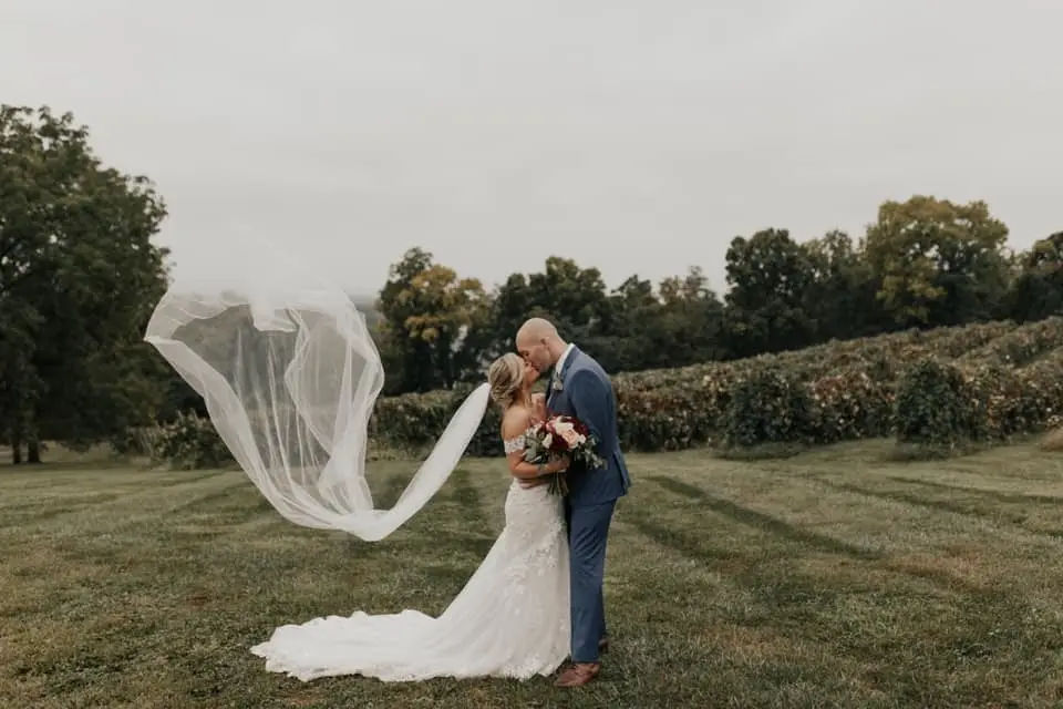 Bride and groom kissing in a vineyard as the bride's long veil blows in the wind
