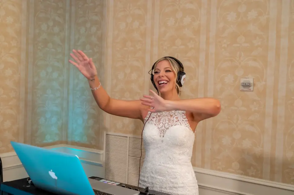 Bride wearing DJ headphones and smiling with arms out at the DJ laptop