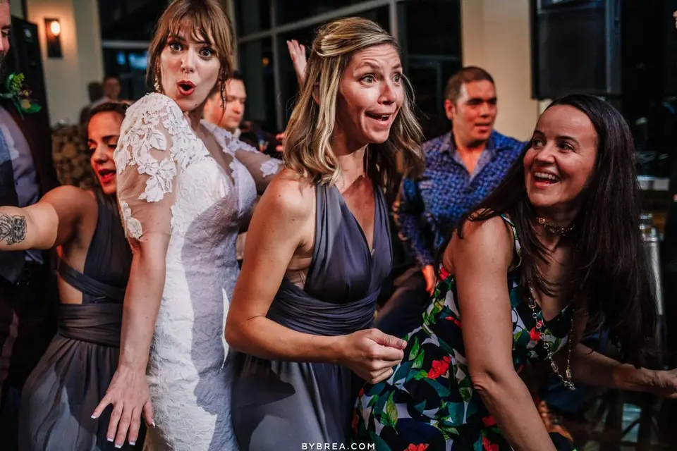 Bridesmaids and a bride in a lace gown making playful faces while dancing with guests at a wedding reception