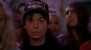 Man in a Wayne's World cap looking wide-eyed in a crowd, in a movie reaction GIF still