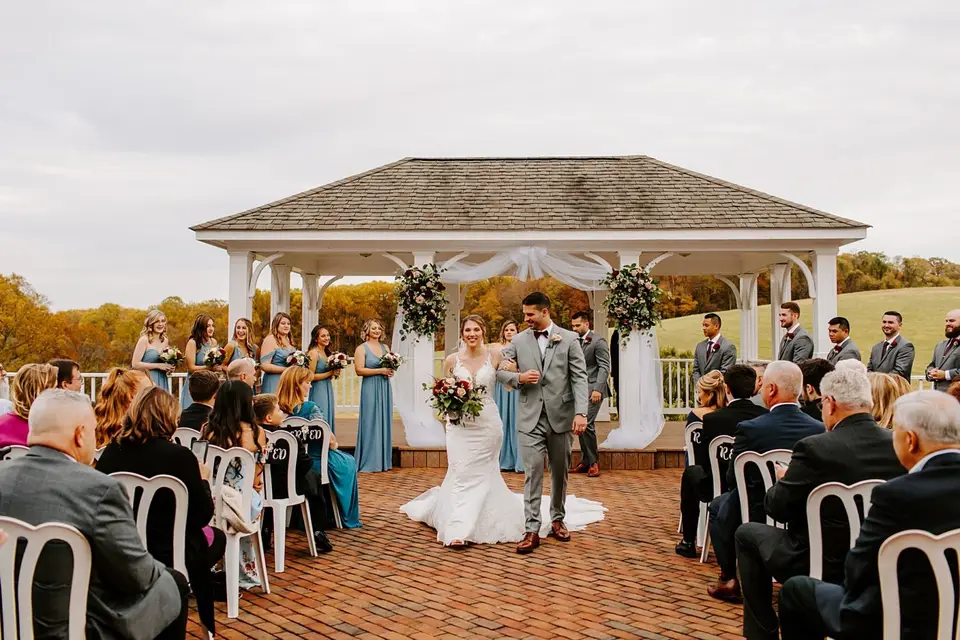 Bride and groom walking up the aisle past guests at a gazebo with bridesmaids and groomsmen behind