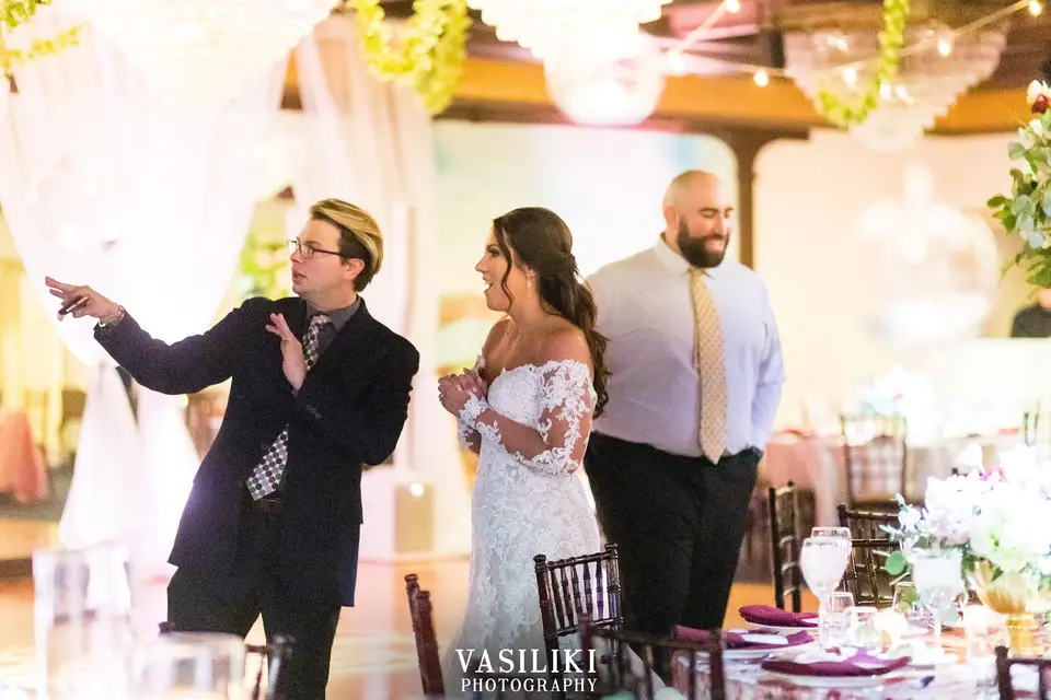 Man in a blazer pointing out something to the bride at a reception hall with chandeliers and table settings