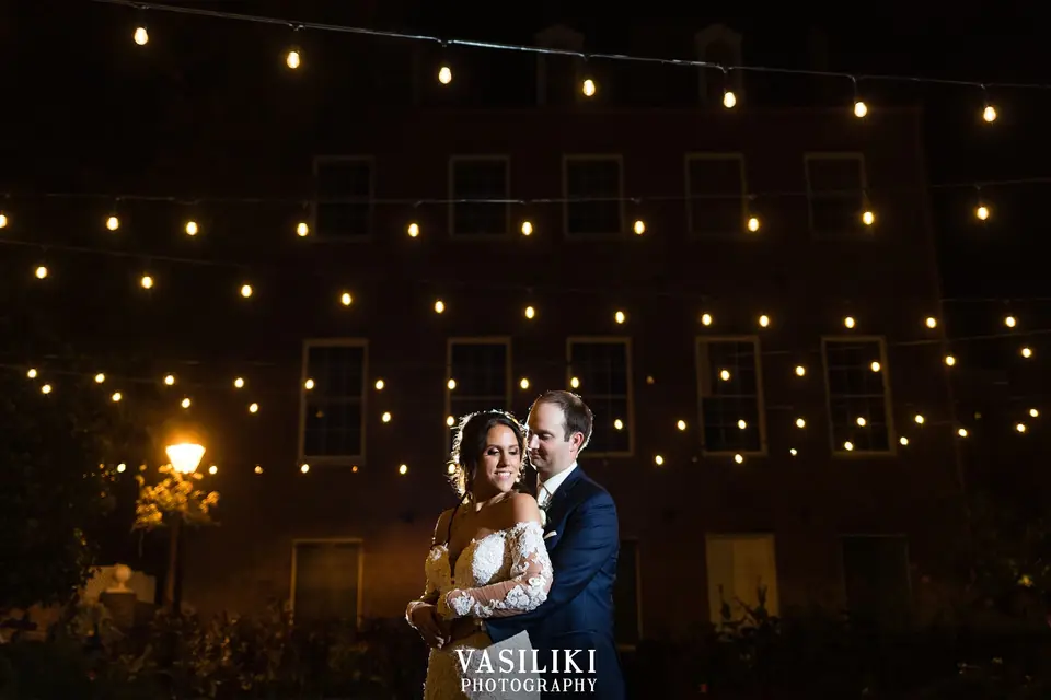 Becky and Matt embracing at night under strung lights in front of a brick building