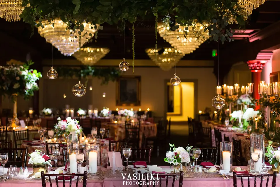 Ballroom reception set with candlelit tables, pink linens and hanging crystal chandeliers at Becky and Matt's wedding
