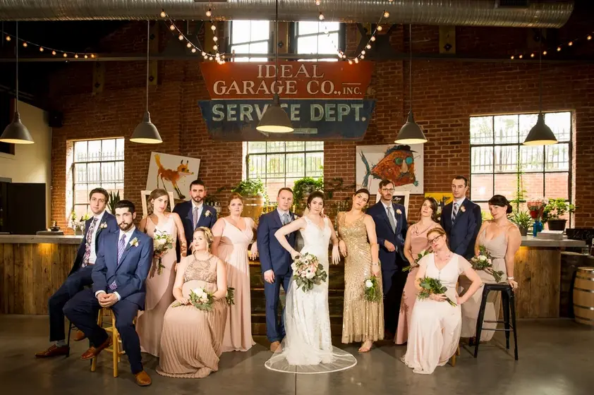 Wedding party posing in a brick industrial venue beneath a vintage Ideal Garage sign