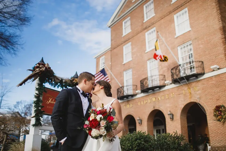 Bride and groom kissing outside a historic red brick inn with holiday garland and a Maryland flag