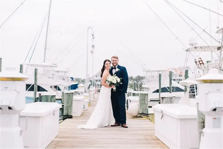 Bride and groom posing together on a wooden marina dock with docked boats behind them