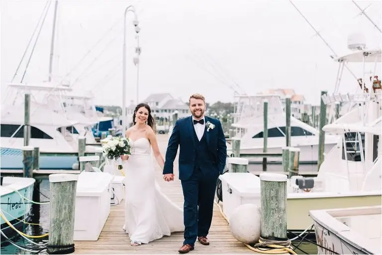 Bride and groom walking hand in hand on a marina dock lined with docked boats
