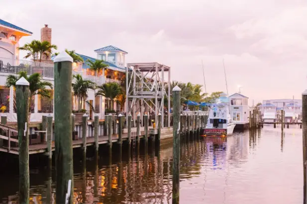 Waterfront boardwalk with pilings, boats and pastel buildings at dusk