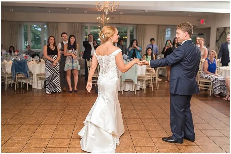 Bride and groom beginning their first dance on a wood floor in a clubhouse ballroom with guests watching