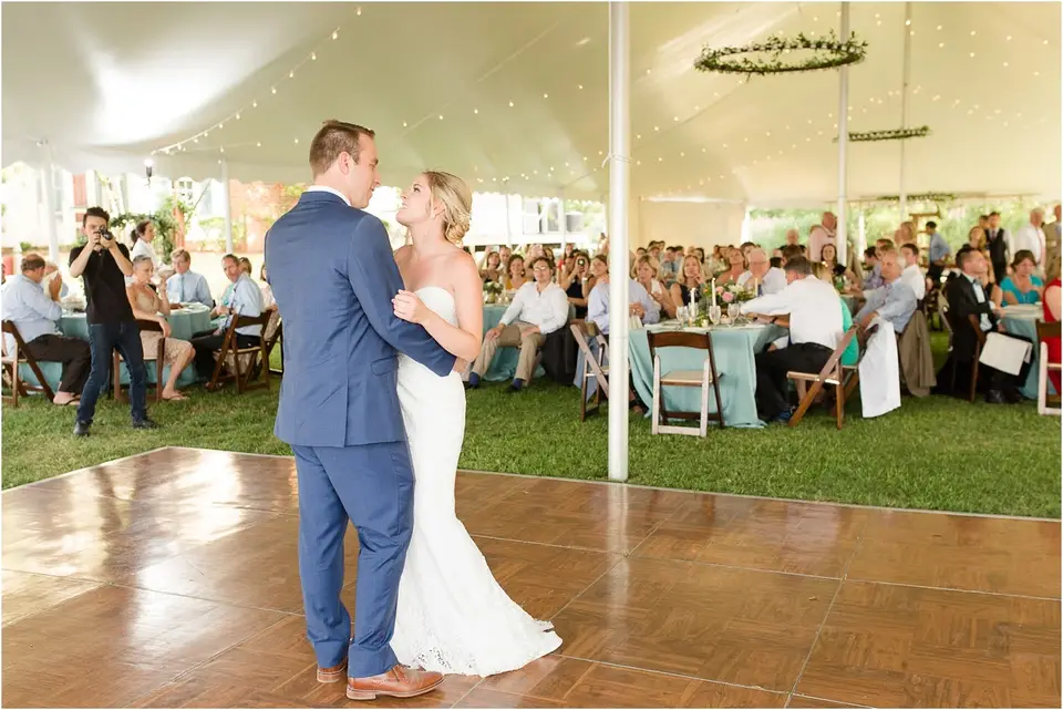 Bride and groom sharing a first dance under a reception tent as guests watch from their tables