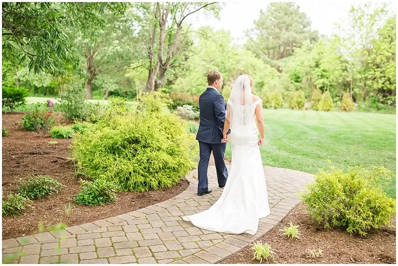 Bride and groom holding hands and walking away on a brick path through a garden