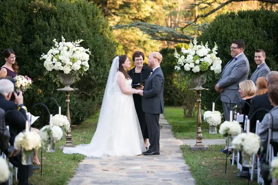 Bride and groom exchanging vows on a garden path with white flower arrangements and seated guests