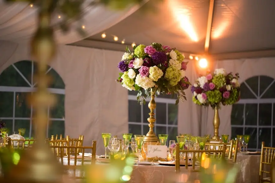 Tall purple, pink and green floral centerpieces on gold stands at a tented reception table