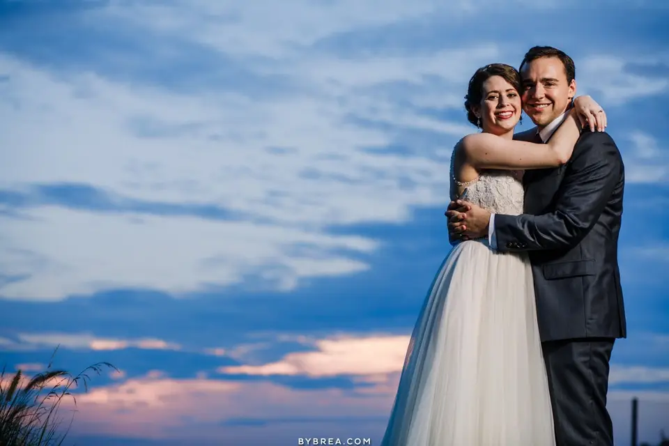 Bride and groom hugging and smiling against a blue and pink dusk sky