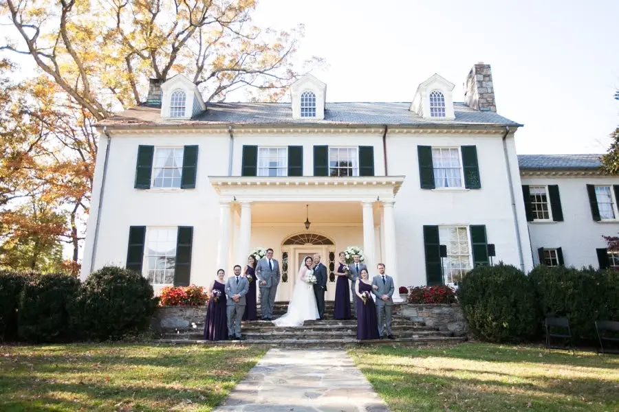 Bridal party lined up on the steps of a white colonial mansion in autumn