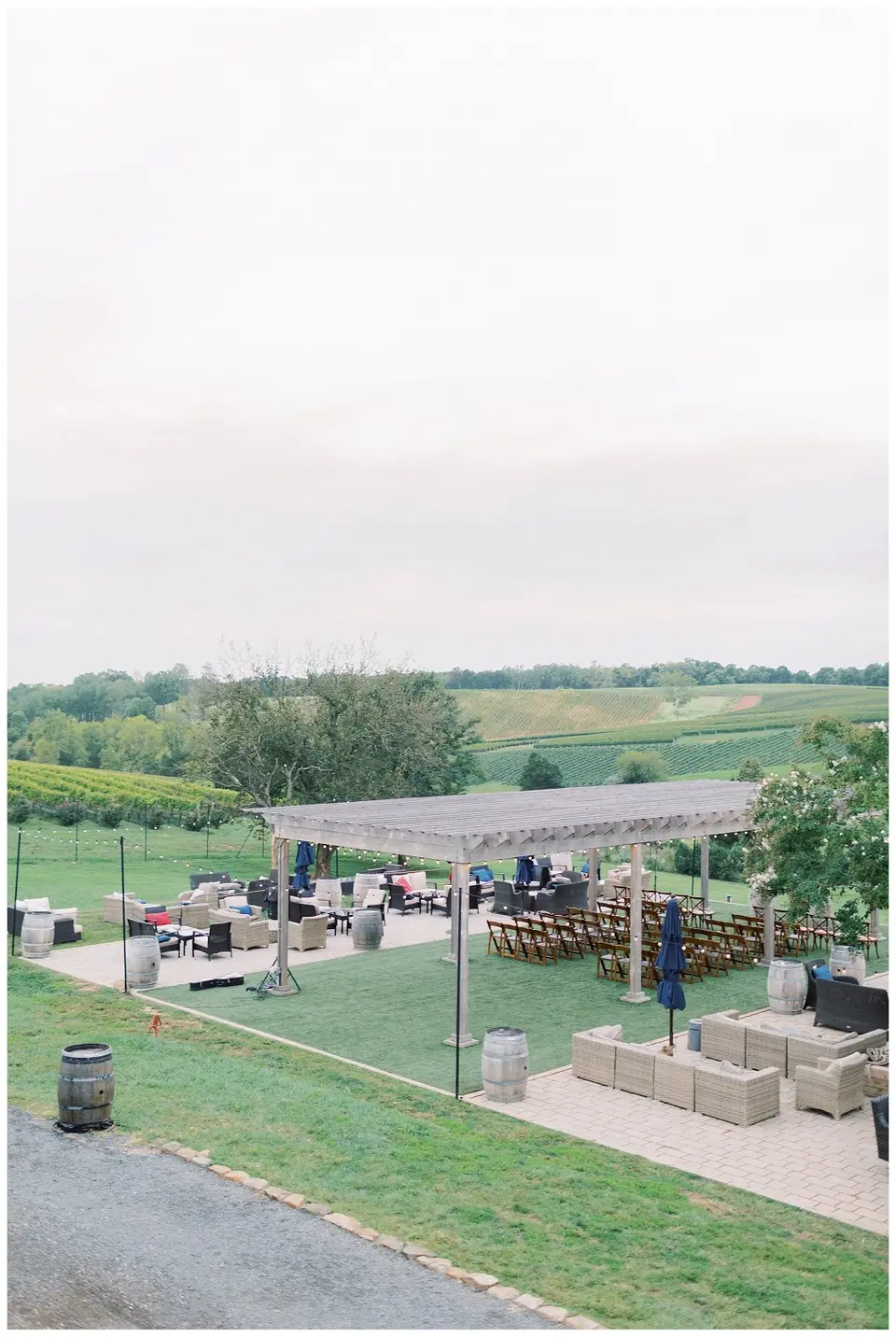 Outdoor ceremony space with a pergola, lounge seating and wooden chairs overlooking vineyards