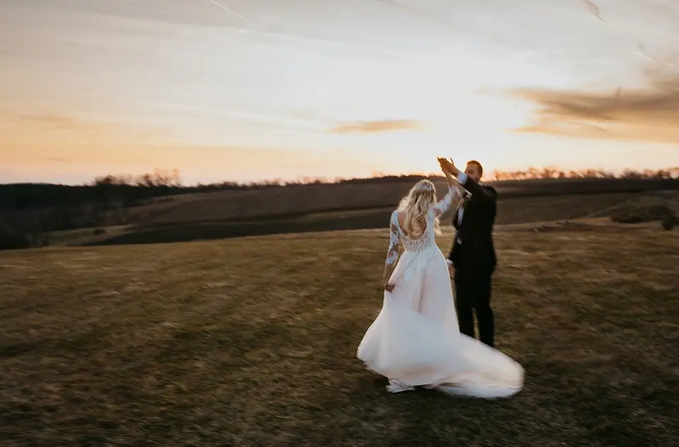 Bride and groom dancing in a field at sunset, her gown flowing