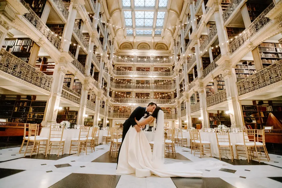 Groom dips the bride between tables set up in the tiered, book-lined George Peabody Library
