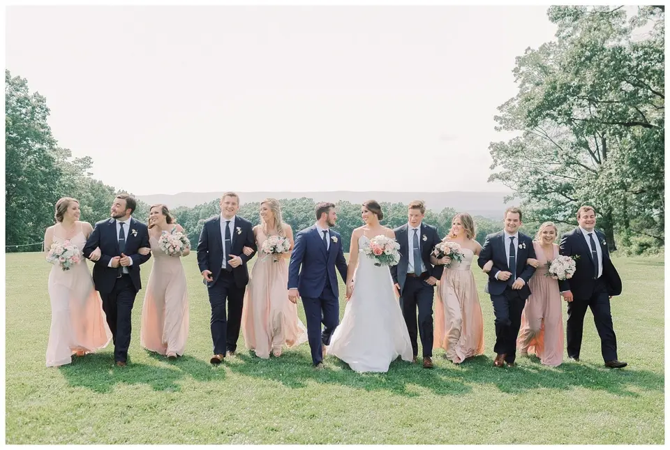 Bride and groom walking arm in arm with bridesmaids in blush dresses and groomsmen in navy suits