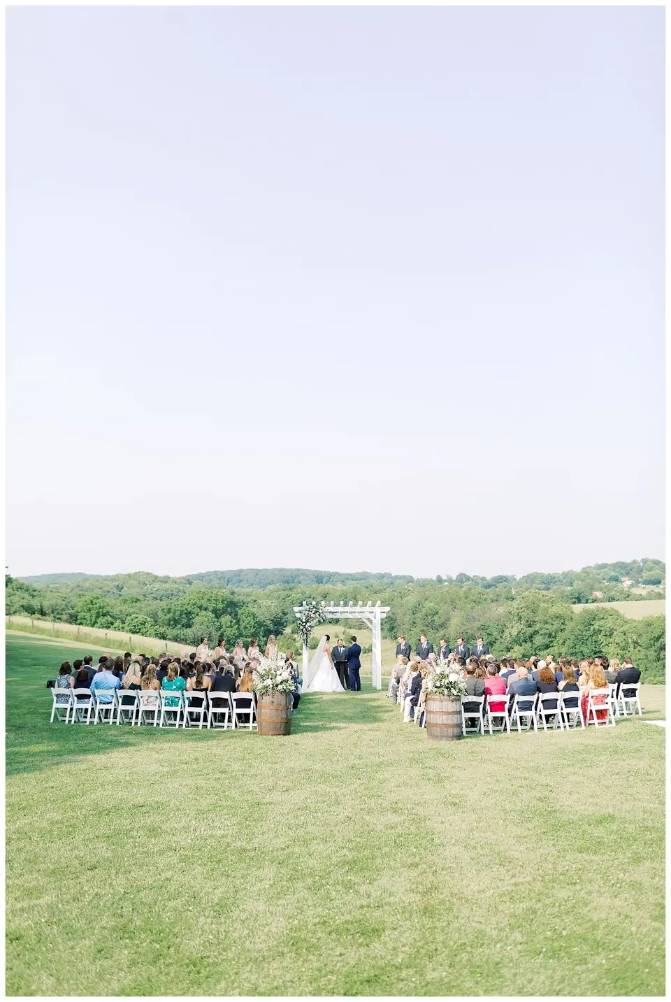 Small wedding ceremony on a grassy hillside with white chairs and a wooden arch