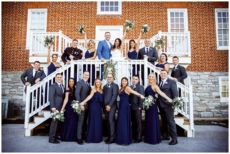 Wedding party in navy attire posed on white porch steps in front of a brick building