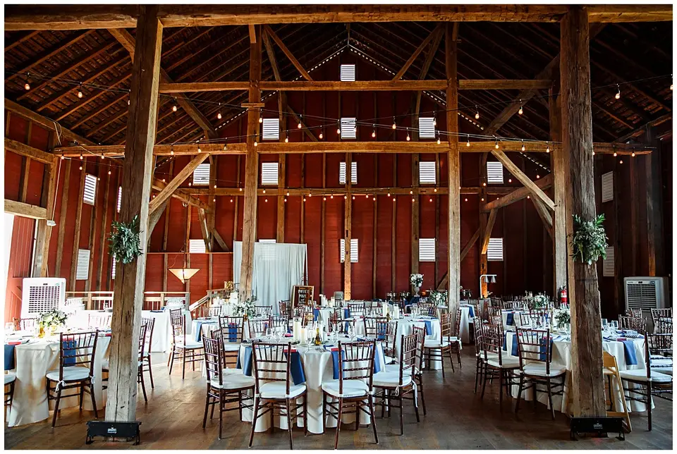 Rustic red barn reception with round tables, string lights and exposed wooden beams