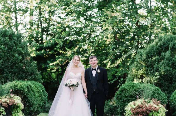Bride and groom standing hand in hand among green hedges in a garden