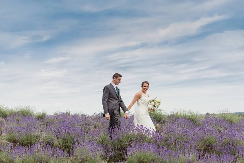 Bride and groom holding hands and walking through a lavender field under a cloudy sky