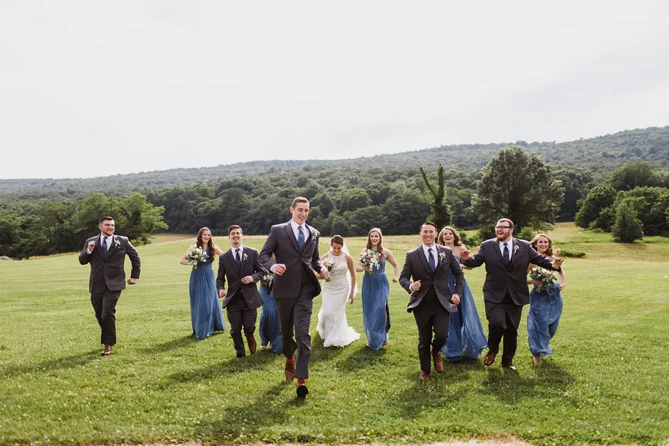 Groomsmen and bridesmaids running across a lawn with the bride and groom behind them