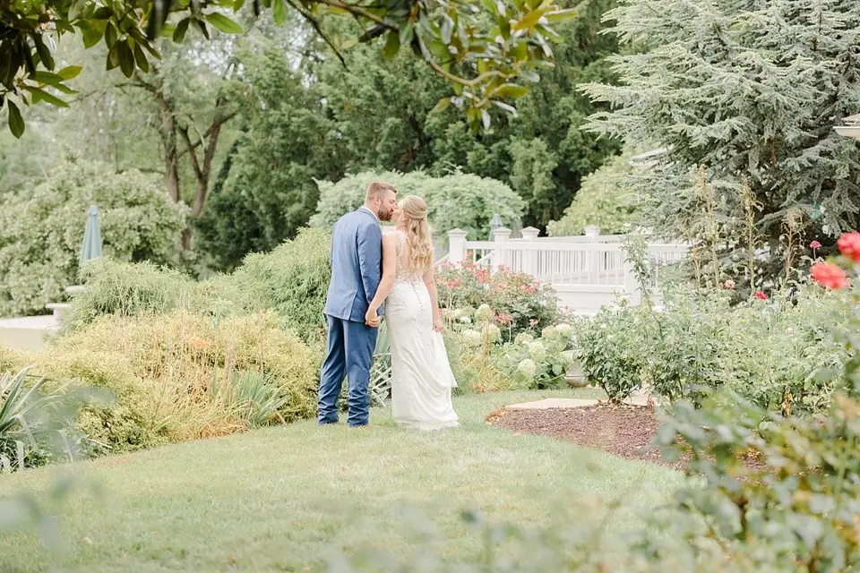 Bride and groom kiss in a landscaped garden with roses and shrubs