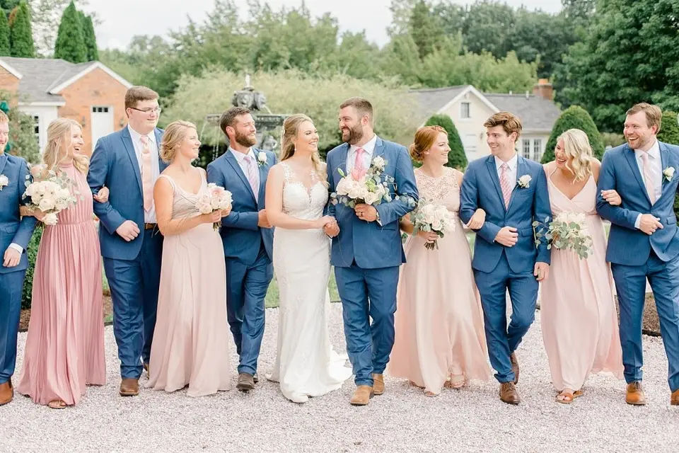 Bride and groom walking arm in arm with bridesmaids in blush dresses and groomsmen in blue suits