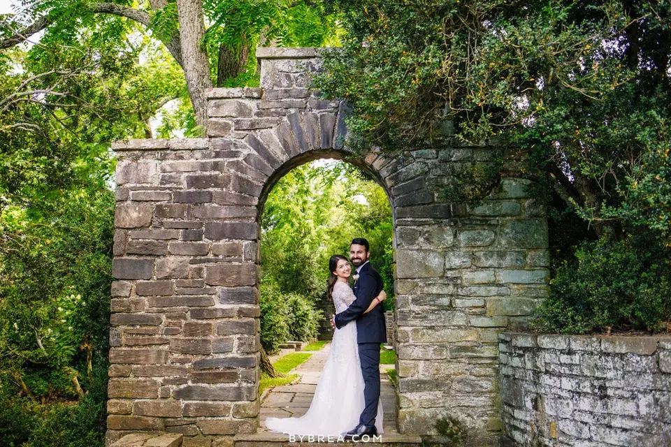 Bride and groom embrace in a stone archway surrounded by greenery