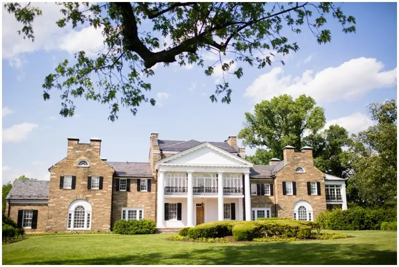 Stone and brick mansion with a white columned portico and green lawn in front
